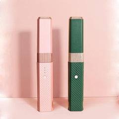 Two rectangular Hair Wand Pro devices in pink and green with textured grips and buttons against a soft pink background