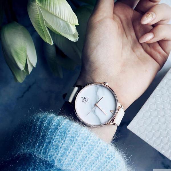Shengke Fashion Watch for Women with marble dial and rose gold case worn on wrist with blue sweater background.