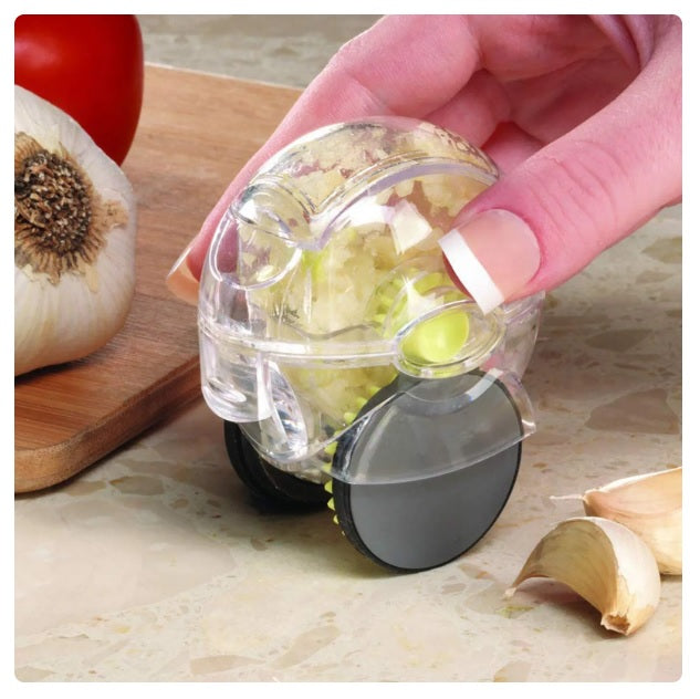 Hand using a clear plastic Rolling Garlic Chopper on a countertop with garlic cloves and a cutting board nearby