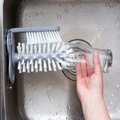 Kitchen Bottle Brush mounted in sink cleaning a glass with multiple angled white bristles and handle.