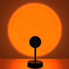 Sunset Lamp casting a warm orange circular glow on a wall, supported by a black stand and base.