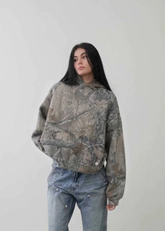 Woman wearing an Urban Camo Retro Hoodie in muted camouflage print paired with blue denim jeans against a plain background.