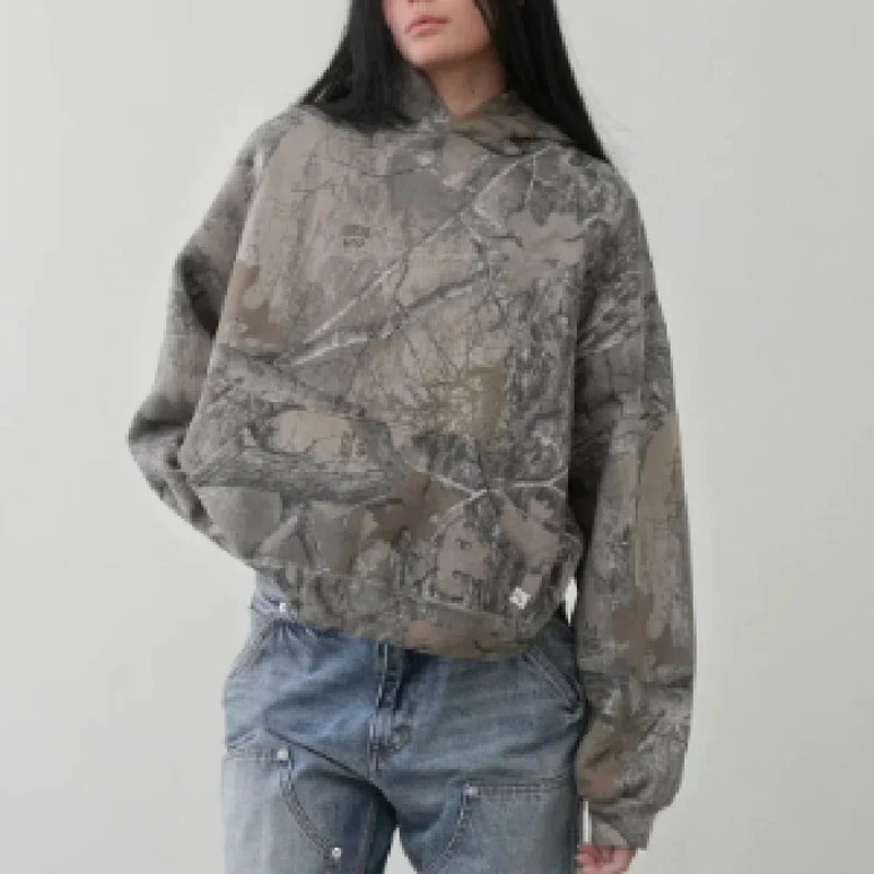 Model wearing a loose fit Camouflage Streetwear Hoodie with a tree branch pattern and blue denim jeans.
