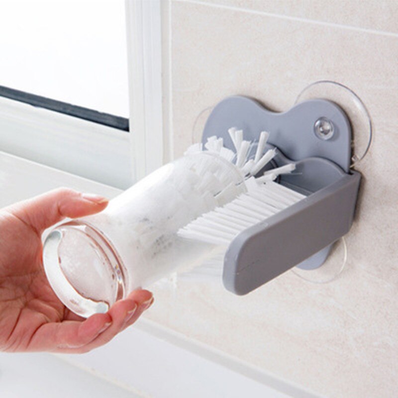 Hand using a Kitchen Bottle Brush with a gray holder attached to a tiled wall to clean a glass bottle.