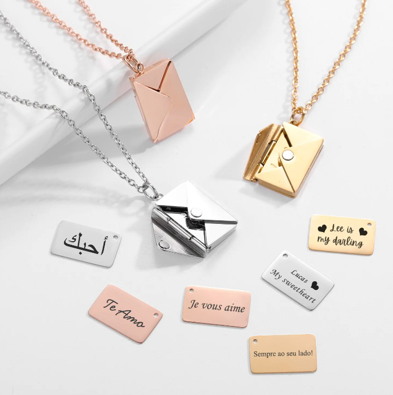 Envelope Necklace in gold, rose gold, and silver with customizable message plaques in multiple languages.
