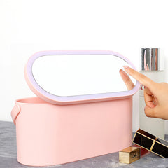 Hand adjusting light on oval mirror attached to pink Makeup Organizer Box with cosmetic items nearby.