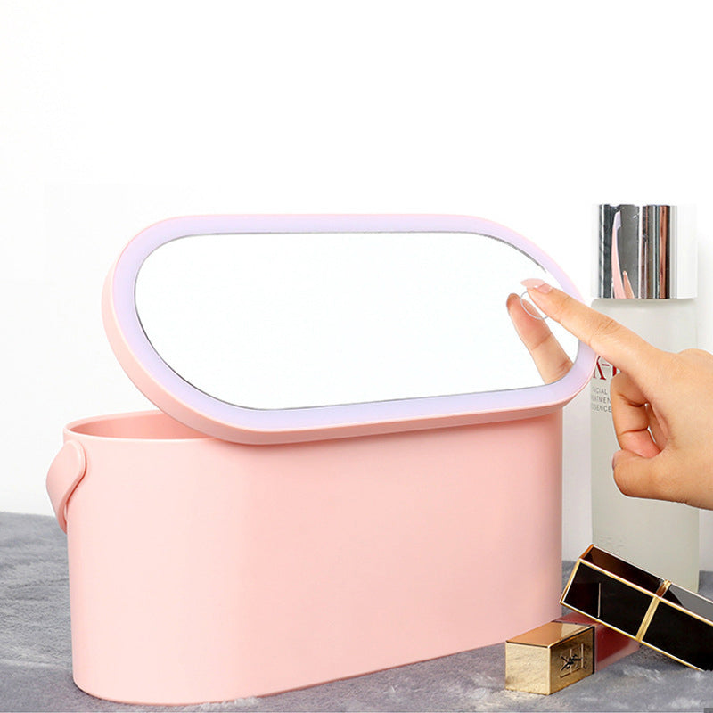 Hand adjusting light on oval mirror attached to pink Makeup Organizer Box with cosmetic items nearby.