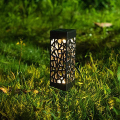 Solar Powered Waterproof Vintage Garden Light glowing at night on grass with decorative cutout metal design.