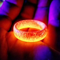 Unisex Luminous Rings glowing bright orange in low light, held in a hand with purple and red lighting background.