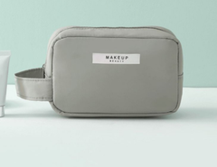 Gray rectangular Makeup Bag with a side handle and a white label on the front against a teal background