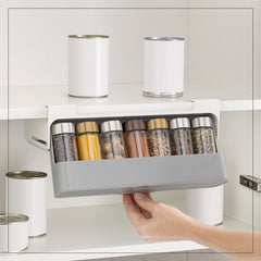Hand installing Kitchen Self-Adhesive Wall-Mounted Spice Organizer holding spice jars under kitchen shelf