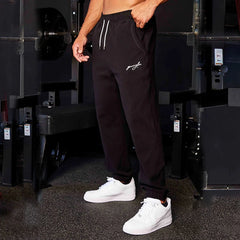 Man wearing black Track Sweatpants with white drawstrings and white sneakers standing in gym environment