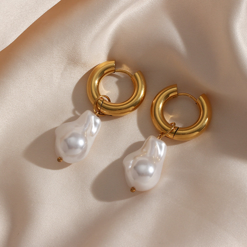 Gold hoop earrings with irregular white pearls designed as Water Drop Earrings on a soft beige fabric background.