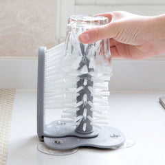 Hand using Kitchen Bottle Brush to clean the inside of an upside-down clear glass on a kitchen countertop.