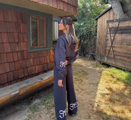 Woman wearing a dark Loose Fit Printed Sweater with matching wide-leg pants standing outdoors near wooden cabins