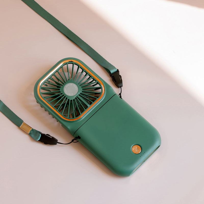Green portable Mini Cooling Foldable Fan with lanyard and power button on a light surface in soft sunlight.