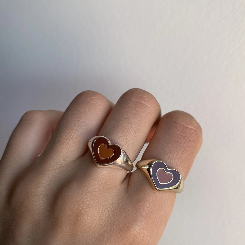 Two hands wearing Creative Love Heart Ring with brown and purple heart designs on gold bands