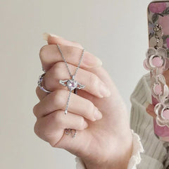Hand holding a silver Heart Wings Necklace featuring a heart-shaped pendant with wing details against a neutral background.