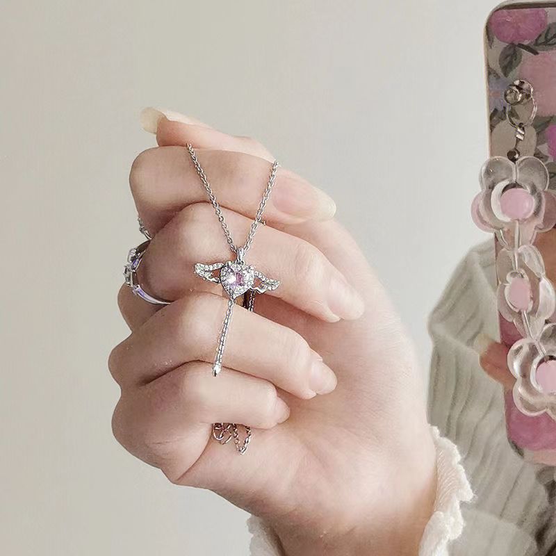 Hand holding a silver Heart Wings Necklace featuring a heart-shaped pendant with wing details against a neutral background.