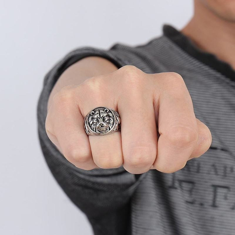 Close-up of a hand wearing a detailed silver Lion Head Rings on the middle finger against a neutral background.
