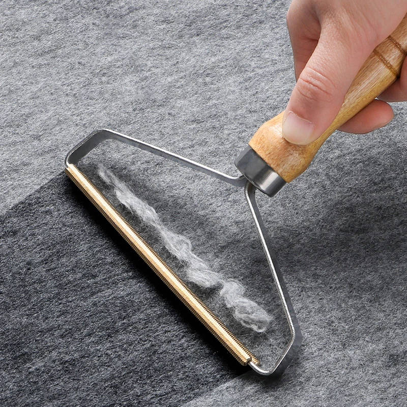 Hand using Pet Hair Remover Brush with wooden handle to remove pet hair from grey fabric surface.