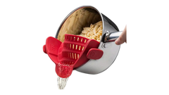 Hand holding pot with red Silicone Pot Strainer attached, draining water from cooked pasta.