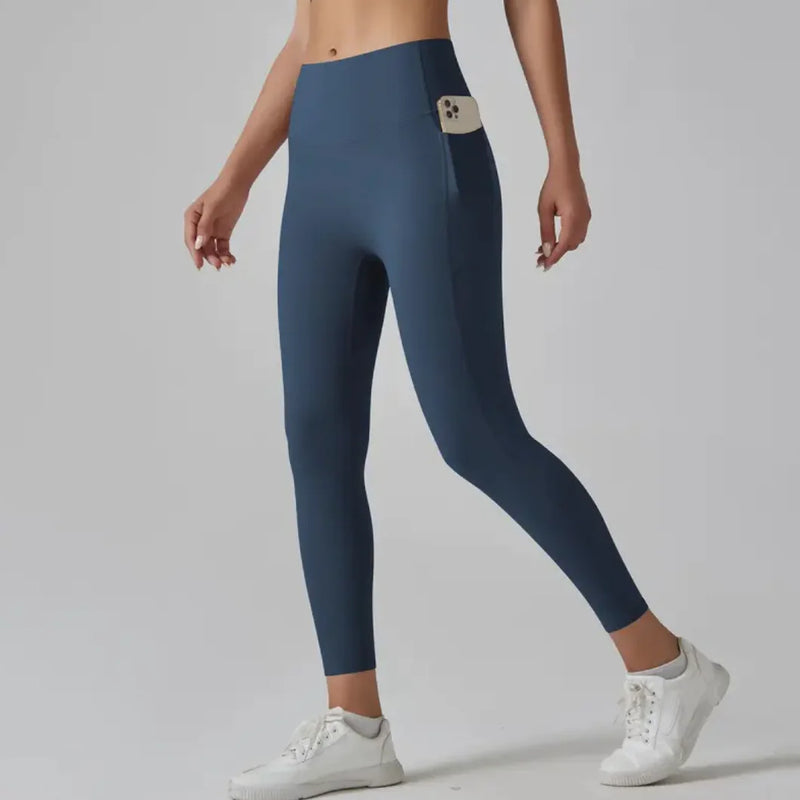 Woman wearing blue High-Waist Fitness Pants with side pocket holding phone, paired with white sneakers