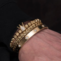 Gold tone Diamond Roman Bracelets with crown and braided designs worn on wrist against black background