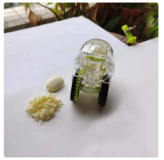 Transparent Rolling Garlic Chopper with black wheels next to whole and chopped garlic on white surface