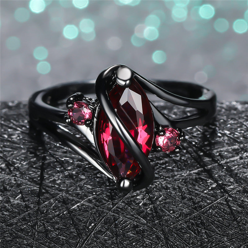 Crystal Ring featuring a marquise red gemstone with two smaller pink stones set in black metal band.